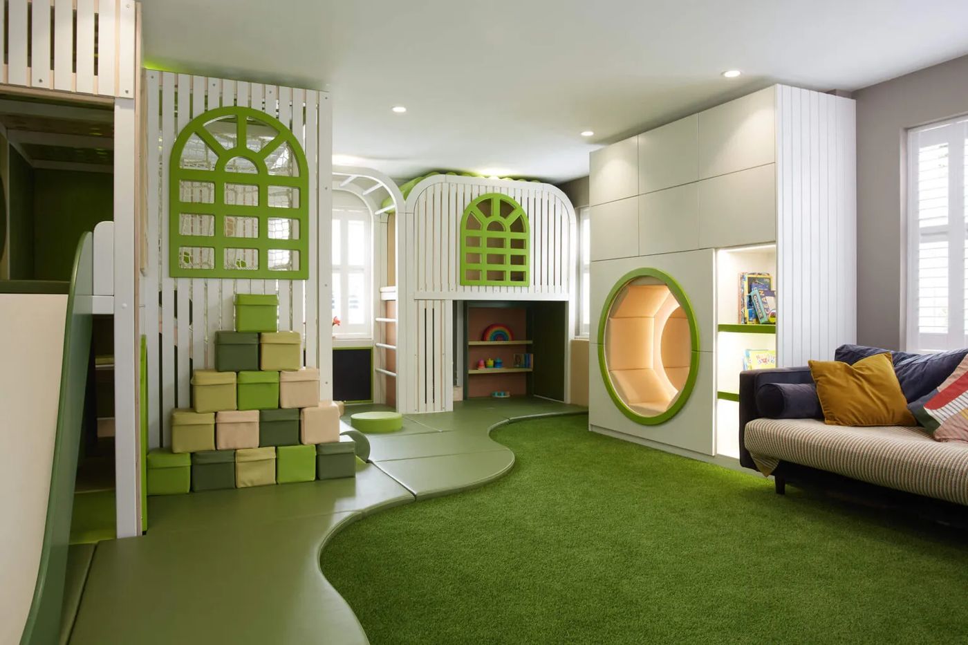 Bright nature-themed indoor playground with white timber playhouses, green accents and a grass play lawn